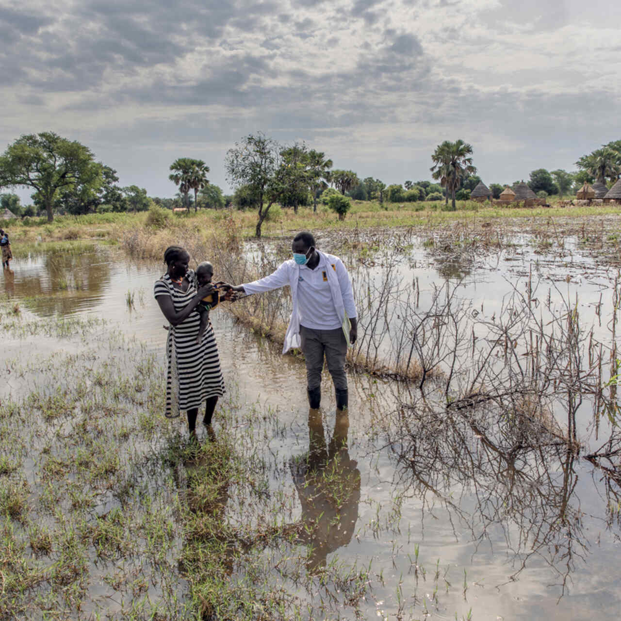 Abuk Deng holds her four year old daughter in her arms as they walk through a flooded field with an IRC malnutrition officer.